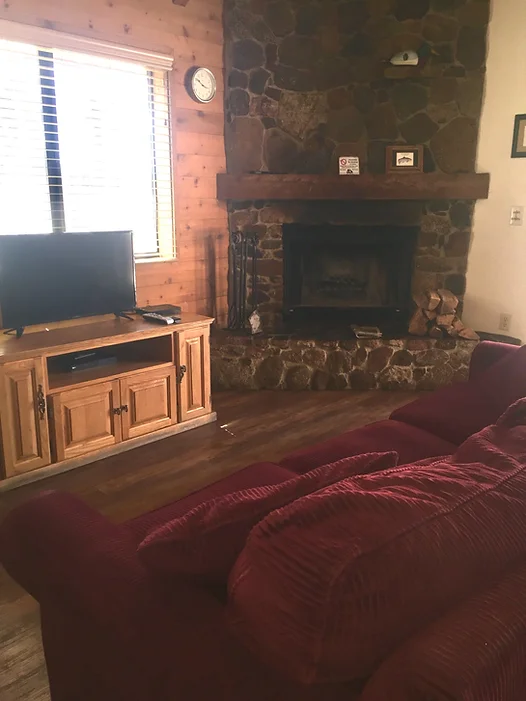 A cozy living room with a stone fireplace, a TV on a wooden stand, and a red couch.