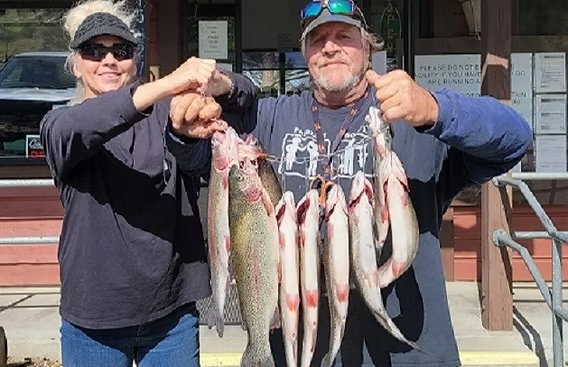 Two people holding several large fish in front of a building, smiling at the camera.