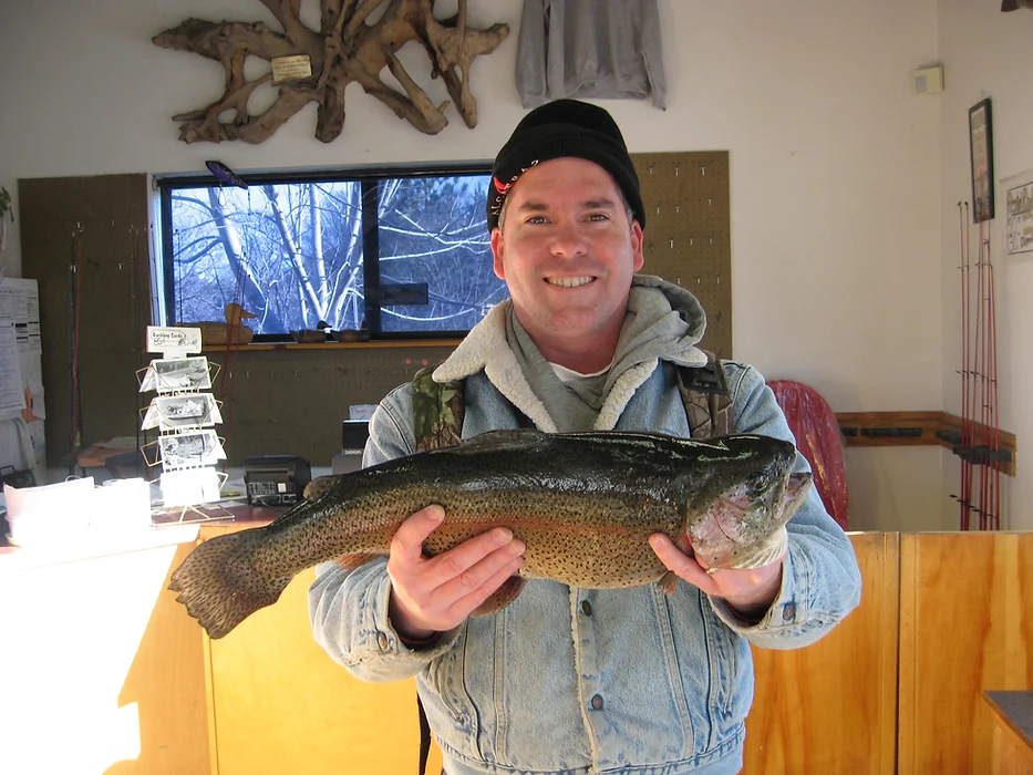 A person smiling, holding a large fish indoors, with wooden decor and a window in the background.
