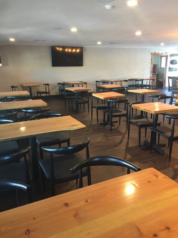 An empty restaurant with wooden tables, black chairs, and a wall-mounted TV.
