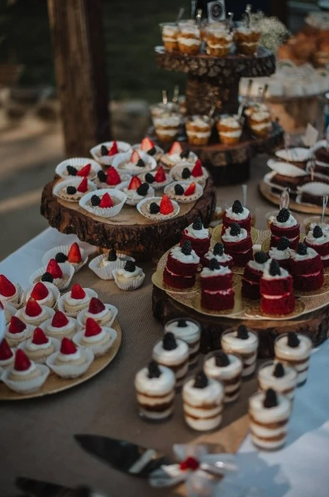An assortment of desserts including cupcakes topped with berries and layered parfaits on rustic wooden stands.