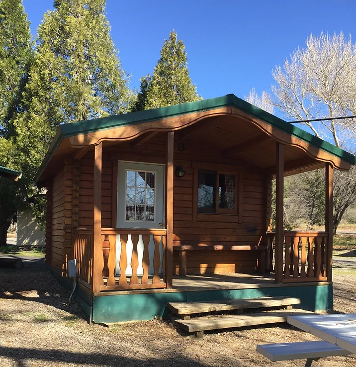A small wooden cabin with a porch, surrounded by trees, under a clear blue sky.
