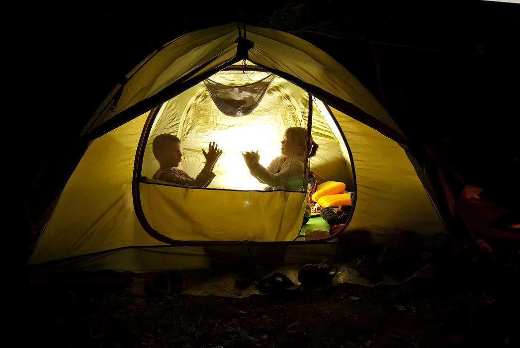 Two kids playing inside a lit tent at night, creating hand shadows.