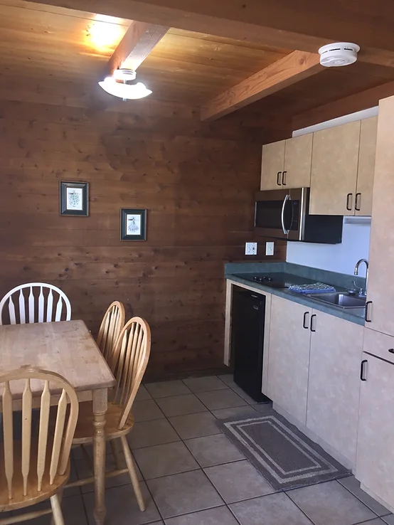 A small kitchen with wooden decor, a dining table with chairs, cabinets, a countertop, and a microwave.