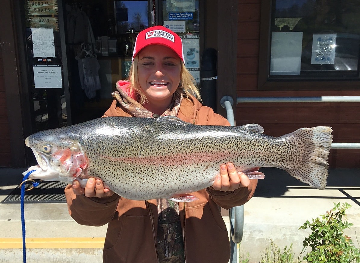 Person holding a large fish outside a building, smiling and wearing a red cap.
