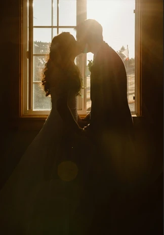 A silhouetted couple kissing in front of a sunlit window.