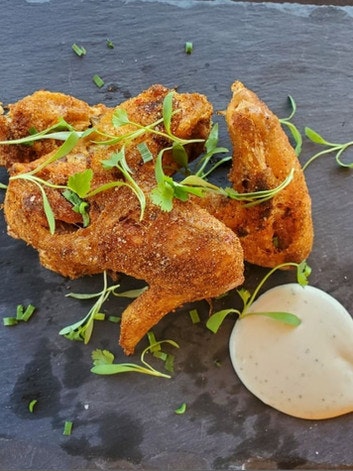 Fried chicken wings garnished with greens, served on a slate with a side of dipping sauce.
