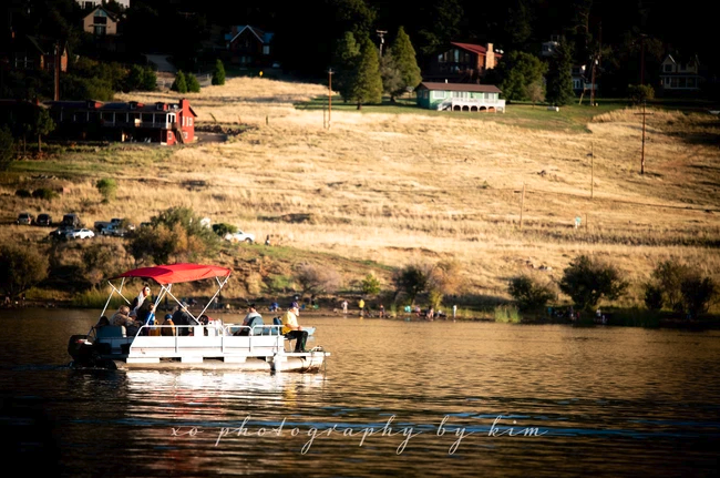 A boat with a red canopy on a calm lake, with a hillside and houses in the background.