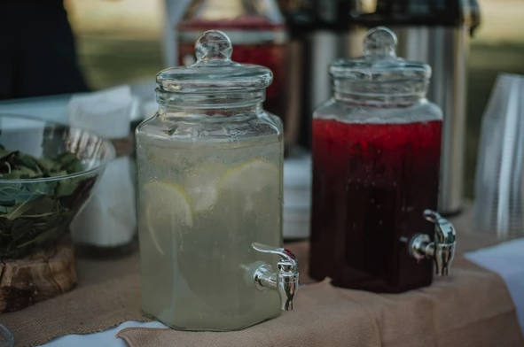 Two beverage dispensers with lemonade and tea, surrounded by cups and napkins on a table.