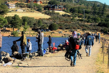 People fishing by a lake, with houses and hills in the background.