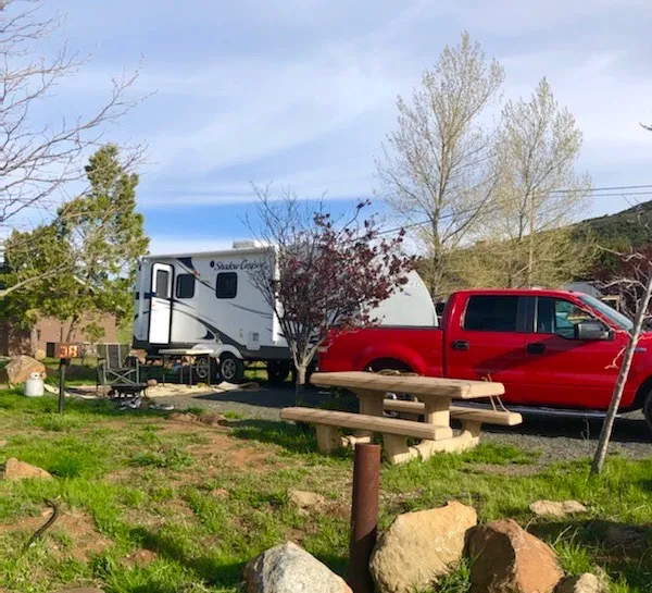 A red truck and travel trailer parked in a grassy area with a picnic table nearby.