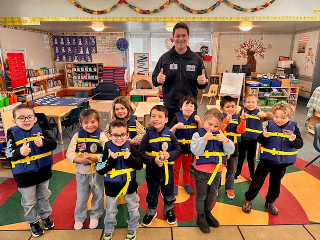 A group of children with an adult in a classroom, all wearing martial arts belts and posing cheerfully.