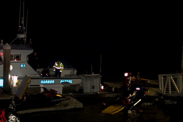 Nighttime view of a harbor patrol boat and jet skis with reflective safety gear visible.