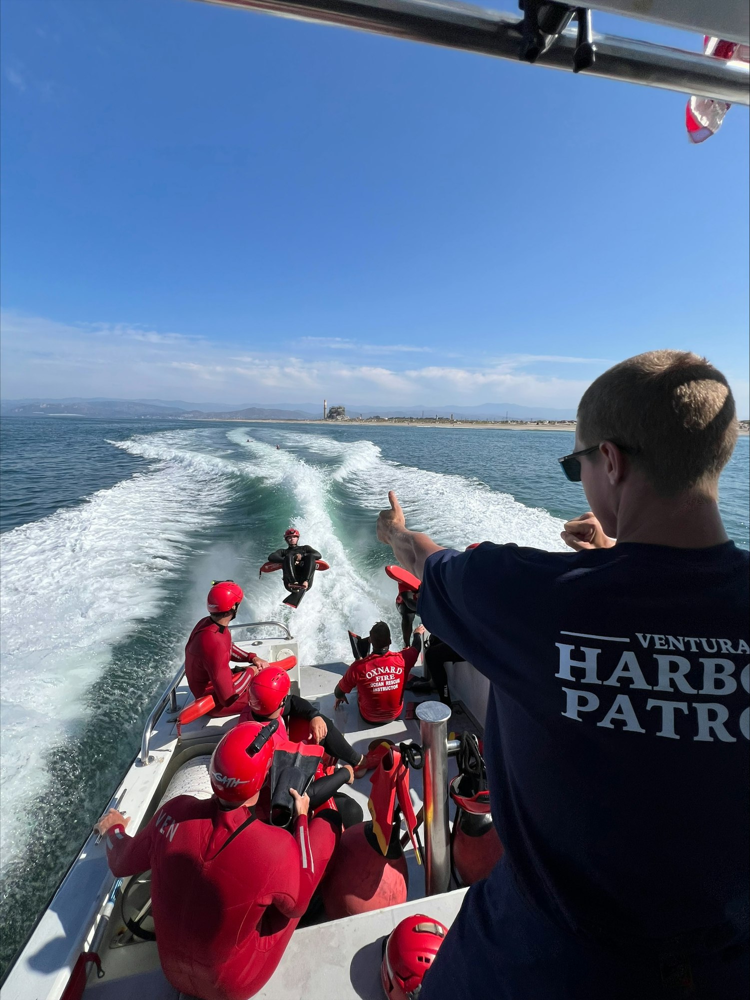 People in red suits are on a boat, with one person in the water being assisted or monitored by the group.
