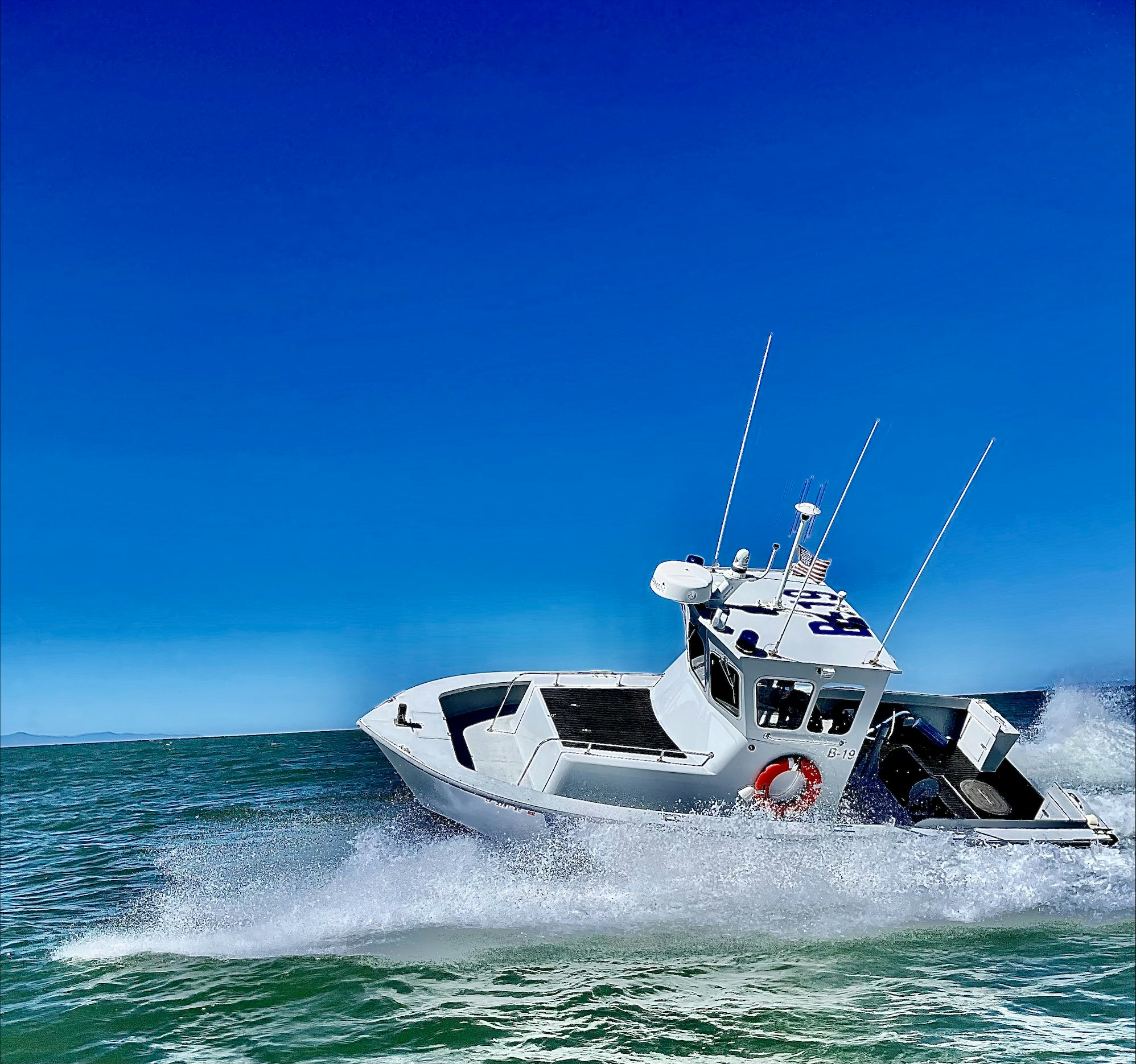 A white motorboat speeding on the ocean, creating a splash against a clear blue sky.