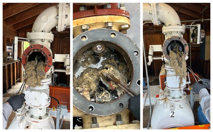 Worker removing debris from a large industrial pipe, likely a sewage pipe, using tools in a wooden-structured building.