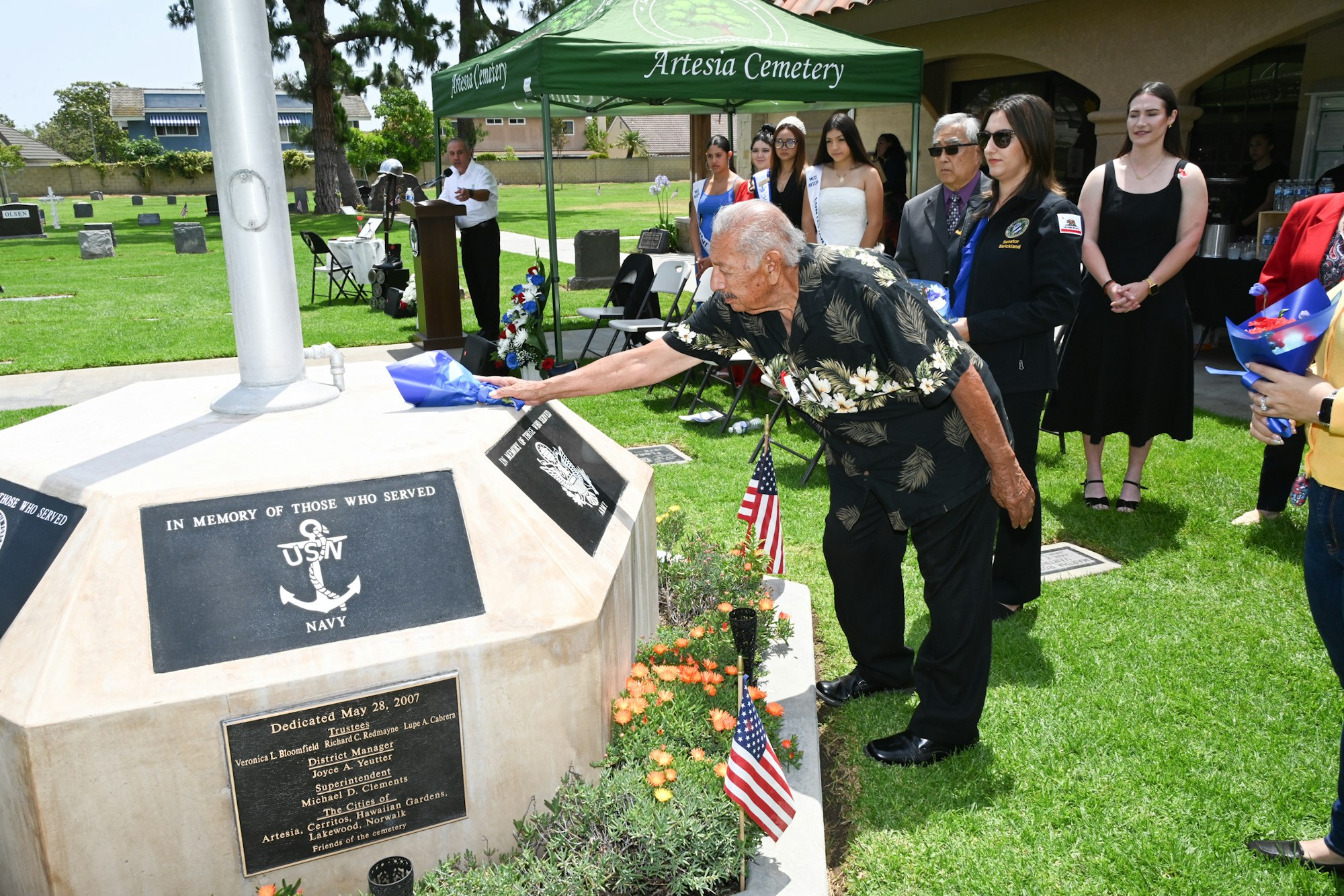A ceremony at a cemetery with attendees honoring veterans, featuring a touching moment at a memorial.