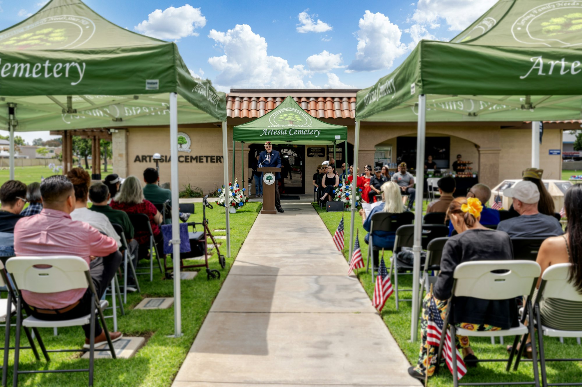 A gathering at Artesia Cemetery, featuring a speaker and an audience under tents, honoring and remembering those who have passed.