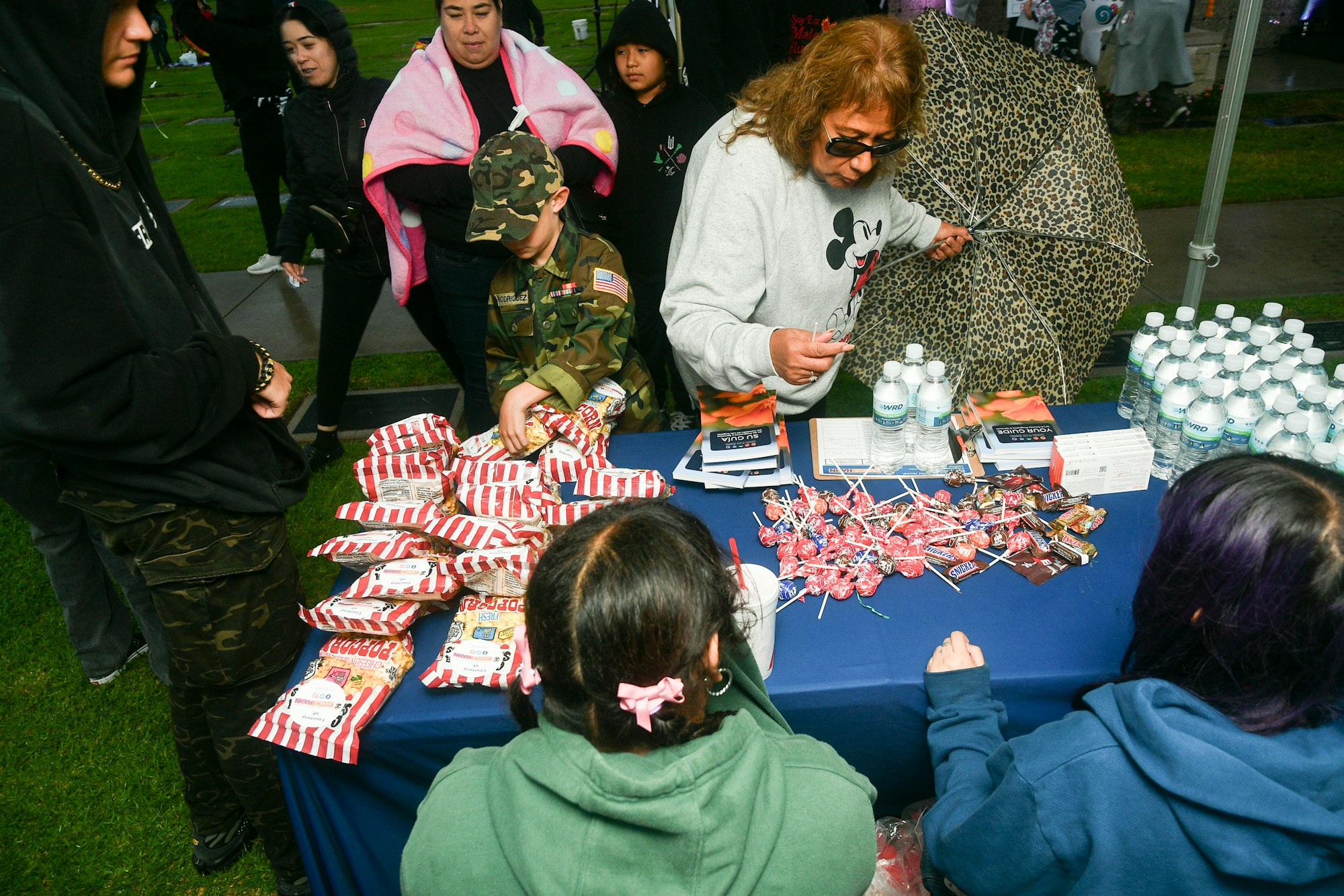 People at a table with snacks, water bottles, and leaflets, possibly at an outdoor event or distribution.
