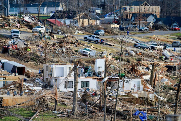 Devastation after a disaster, with damaged buildings, debris, and vehicles.