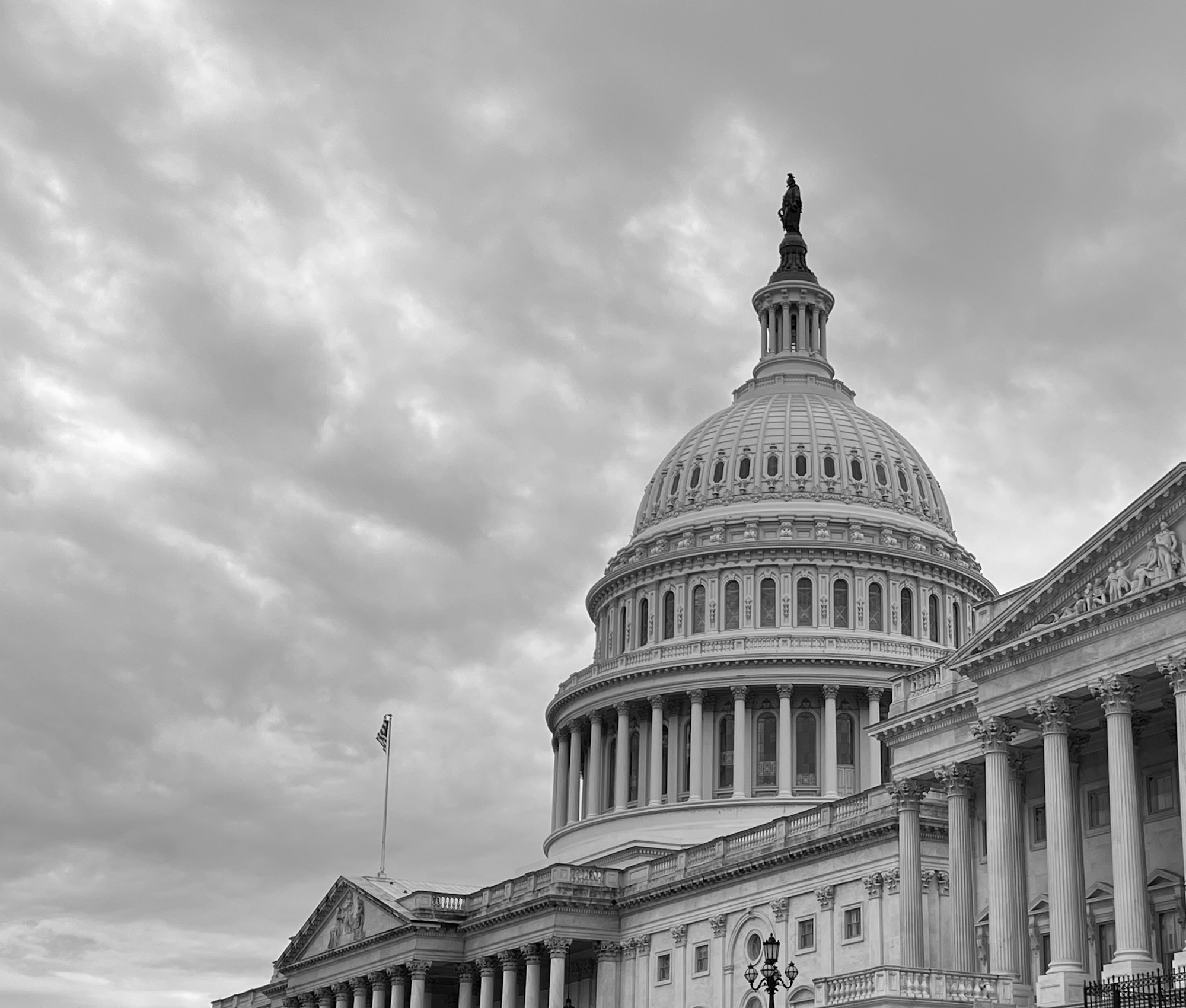 Black and white photo of the US Capitol Building under a cloudy sky.