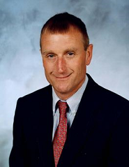 Man in dark suit coat, blue dress shirt, and red tie