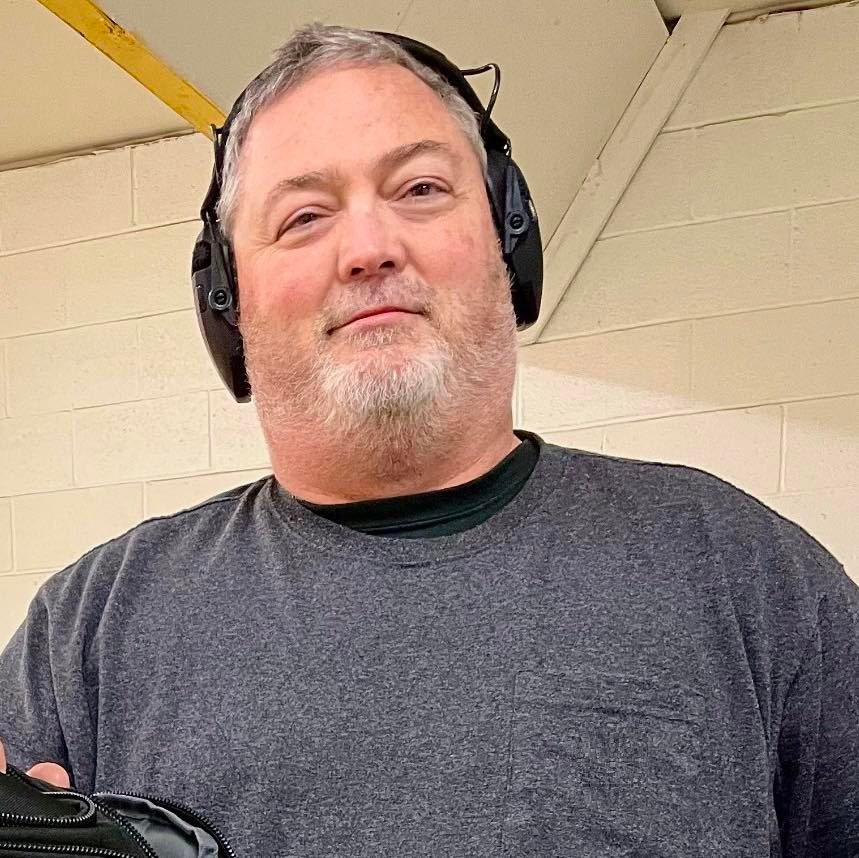 Man in gray tee shirt with gun firing range ear protection