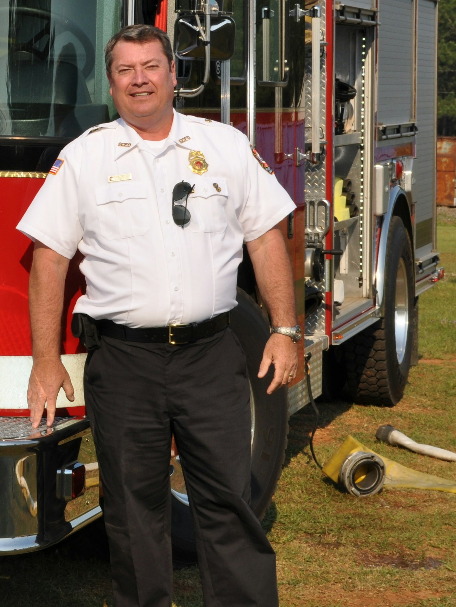 Man in white shirt fire chief's uniform standing in front of a fire truck