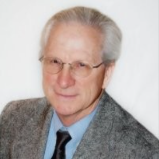 An elder man with glasses, wearing a tie and blazer.