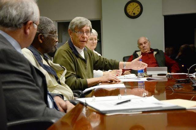People sitting at a long table having a discussion with paperwork on the table in front of each person.