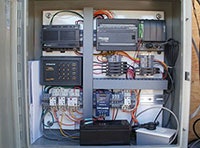 An electrical control panel with various components, wires, and connectors organized inside a metal enclosure.