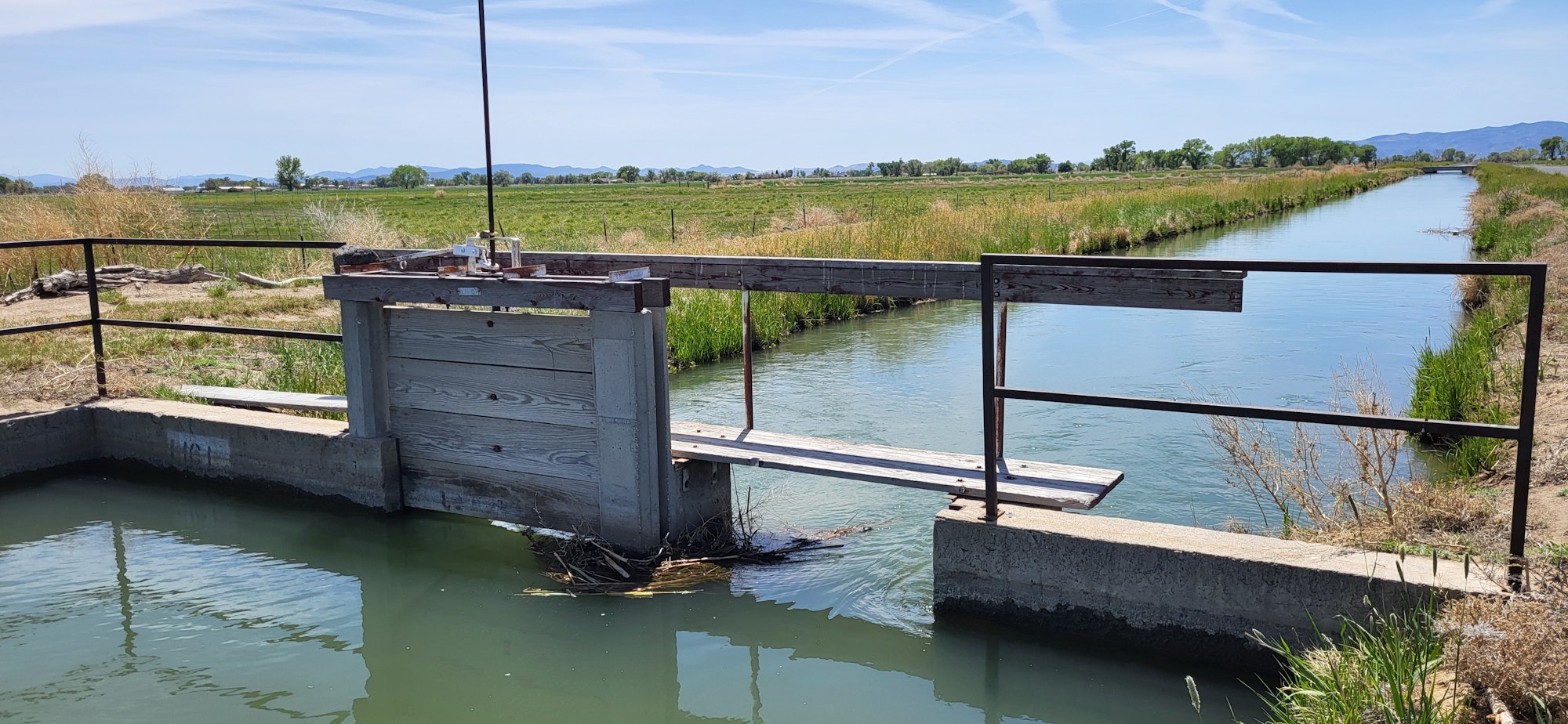 A water canal with a wooden and concrete sluice gate in a rural landscape.