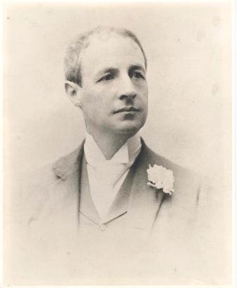 A black-and-white portrait of a man wearing a suit with a flower in the lapel.