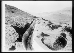 A desert landscape with a trench or canal cutting through sandy terrain under a clear sky.