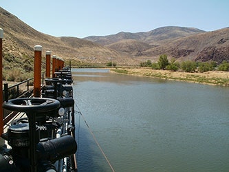 A waterway with machinery on the left, surrounded by rolling hills and sparse vegetation.