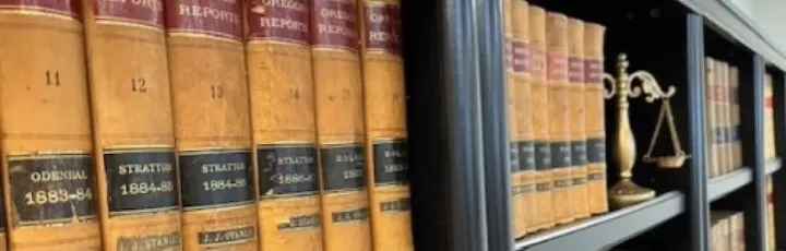 A bookshelf featuring old law books and a scale of justice, suggesting a legal or historical context.