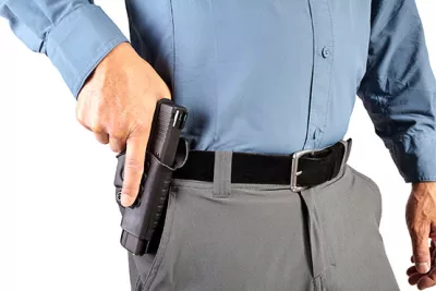 A person in a blue shirt is reaching for a handgun holstered at their waist.