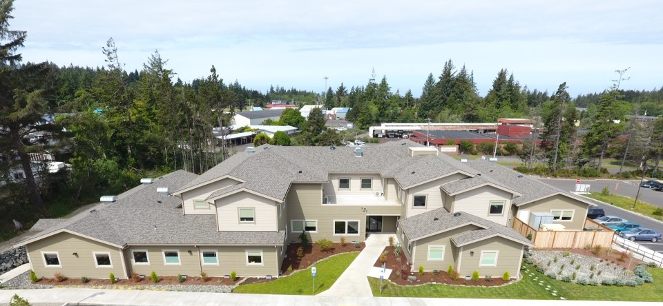The image shows a modern building surrounded by greenery and parking, likely a facility or residential complex.