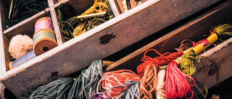A drawer filled with colorful spools of thread, yarn, and skeins, alongside other sewing materials.