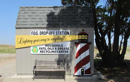 A recycling drop-off station for household fats, oils, and grease, featuring a lighthouse design and a bench outside.