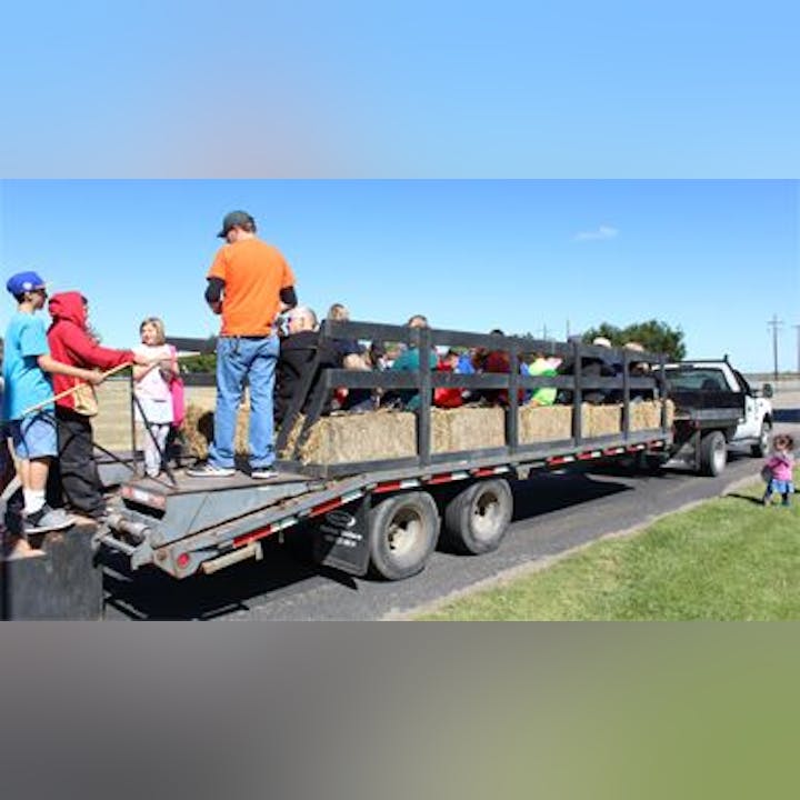 A hayride with children and adults on a trailer filled with hay, parked on a road under a clear blue sky.