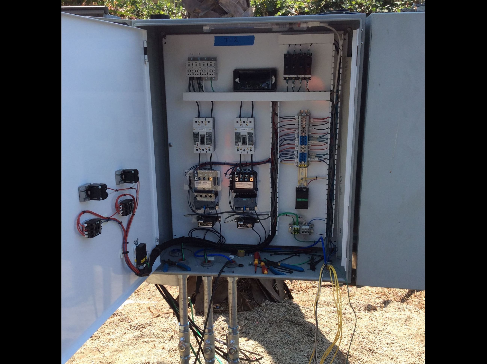 The image shows an open electrical control panel with various components, wires, and tools arranged inside.