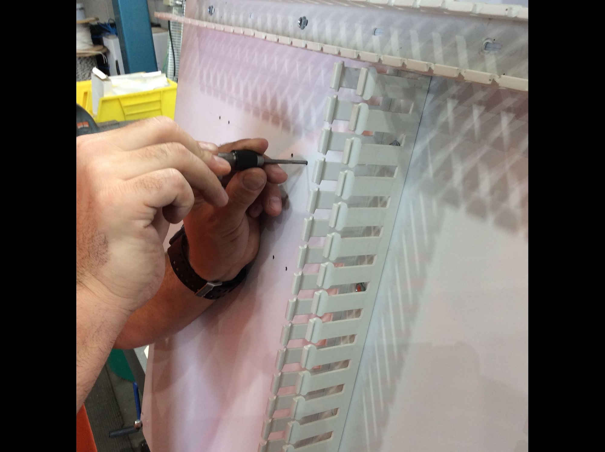 A person is using a screwdriver to tighten or install hardware on a white panel with slots.