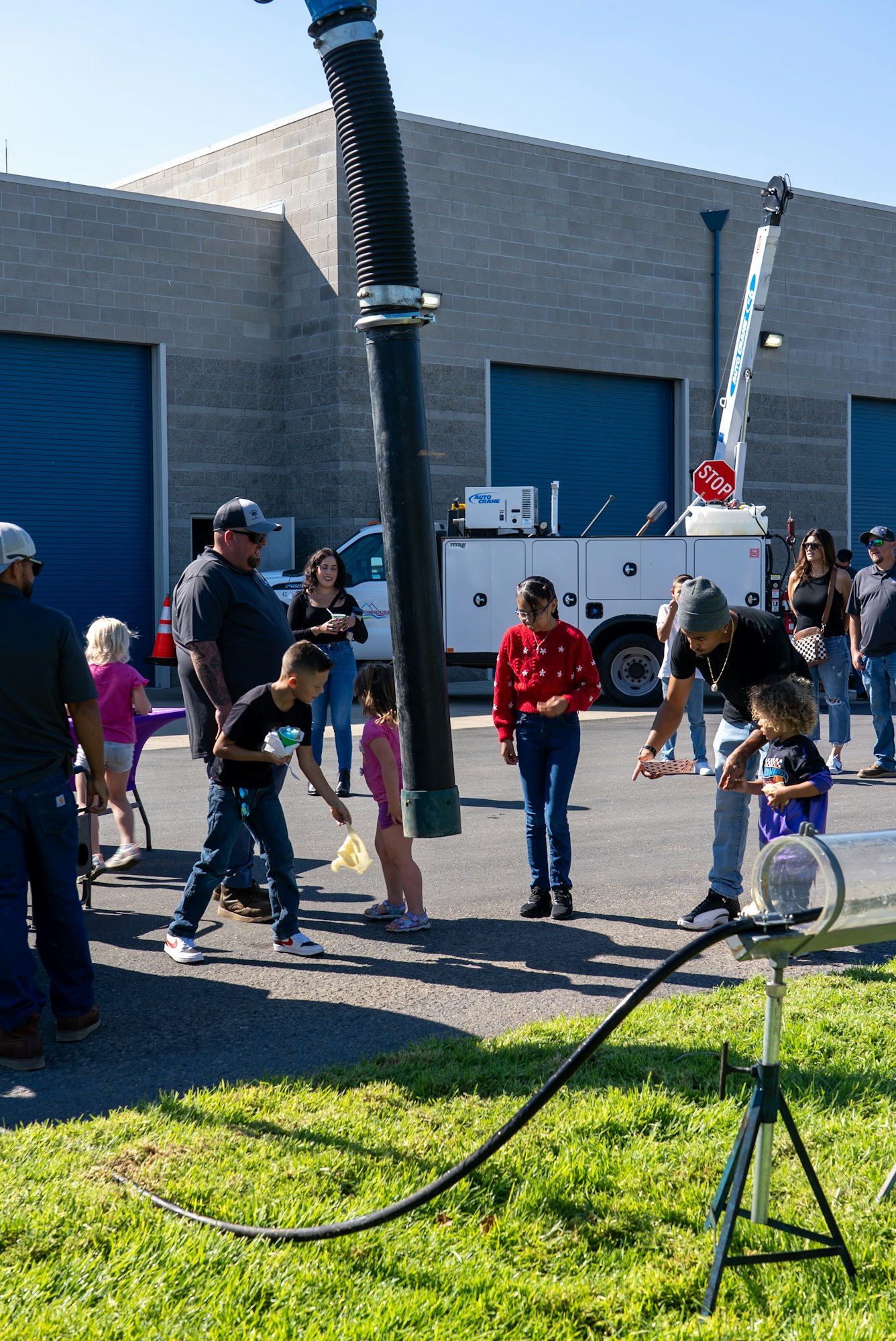 A group of children and adults gather outdoors, engaging with activities and equipment at what appears to be a community event.