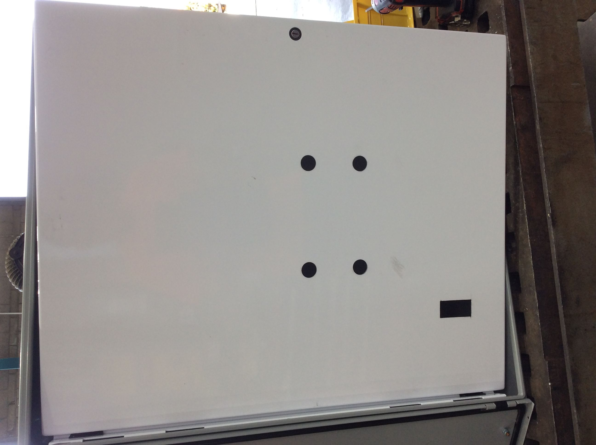 The image shows a plain white panel with four black dots and a small black rectangle, possibly part of an appliance or equipment.