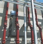 The image shows a wall with several red pipes and metal framework, likely part of a plumbing or industrial system.