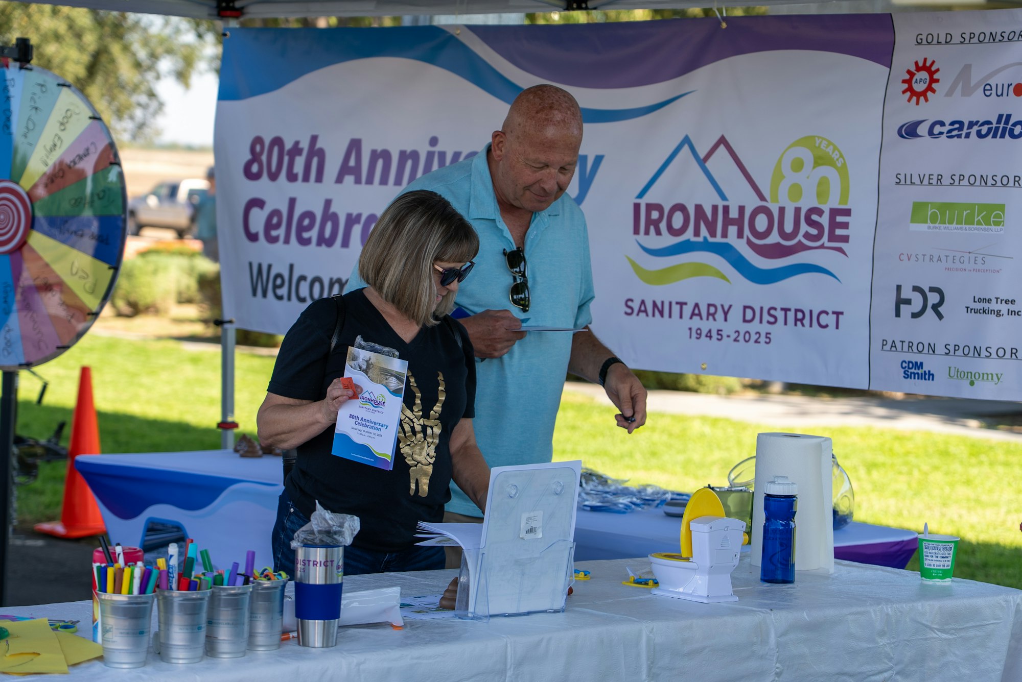 A booth celebrating the 80th anniversary of the Ironhouse Sanitary District, featuring a spinning wheel and informational materials.
