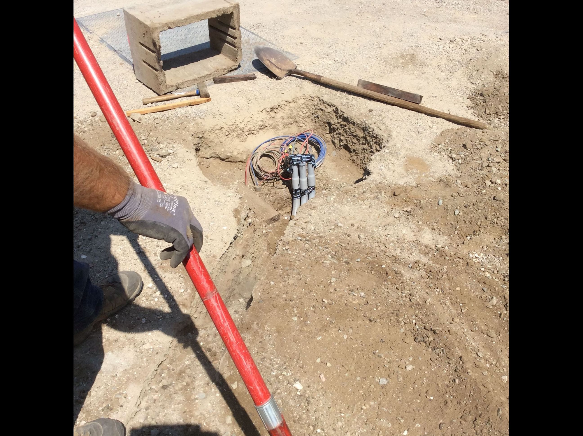 The image shows a construction site with a dug hole, tools, and wires, possibly for utilities or electrical work.