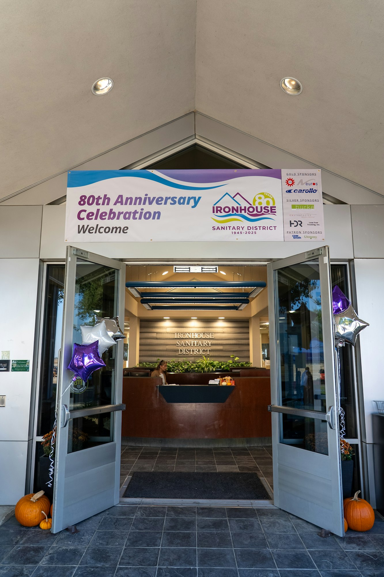 The image shows an entrance celebrating the 80th anniversary of the Ironhouse Sanitary District with balloons and pumpkins.