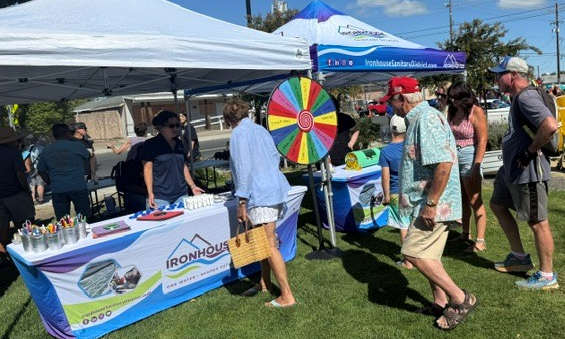 A group of people is gathered around a booth with a spinning prize wheel, promoting a business called Ironhouse.